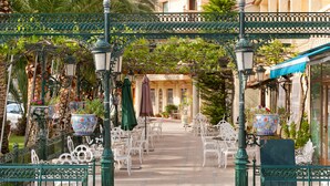 An outdoor café with white metal chairs and tables, green metal railings, and decorative street lamps. - Hotel Rosa (Denia)