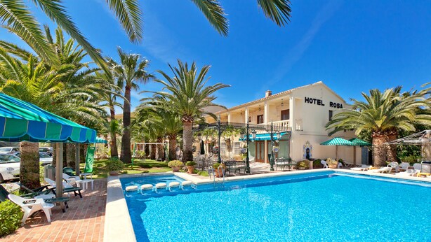 A hotel with a swimming pool, palm trees, and outdoor seating. - Hotel Rosa (Denia)