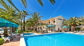 Un hôtel doté d’une piscine, de palmiers et d’un espace extérieur aménagé pour s’asseoir.