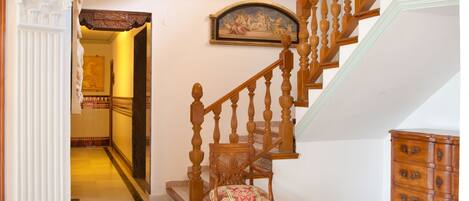 Una imponente escalera con detalles de madera ornamentados, un candelabro y un cuadro enmarcado en la parte superior.