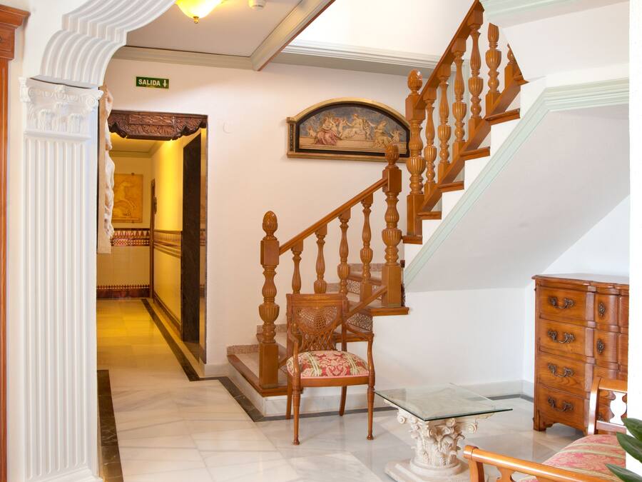 A grand staircase with ornate woodwork, a chandelier, and a framed painting above.