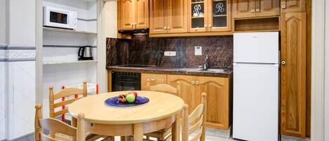 A kitchen with wooden cabinets, a white refrigerator, a microwave, and a dining table with chairs.