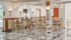 A dining area with multiple tables and chairs, a tiled floor, and wall-mounted lighting fixtures. - Hotel Rosa (Denia)