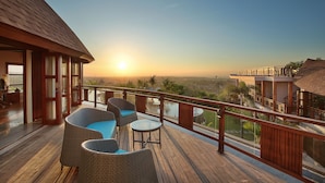 A wooden deck with wicker furniture and a glass balustrade overlooking a scenic view.