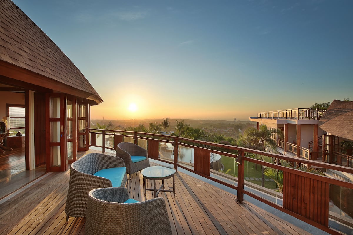 A wooden deck with wicker furniture and a glass balustrade overlooking a scenic view.