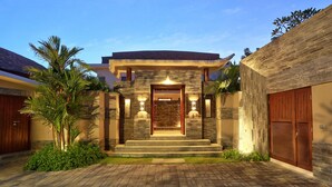 A modern house with a stone facade, a central entrance with steps, and a brick driveway.
