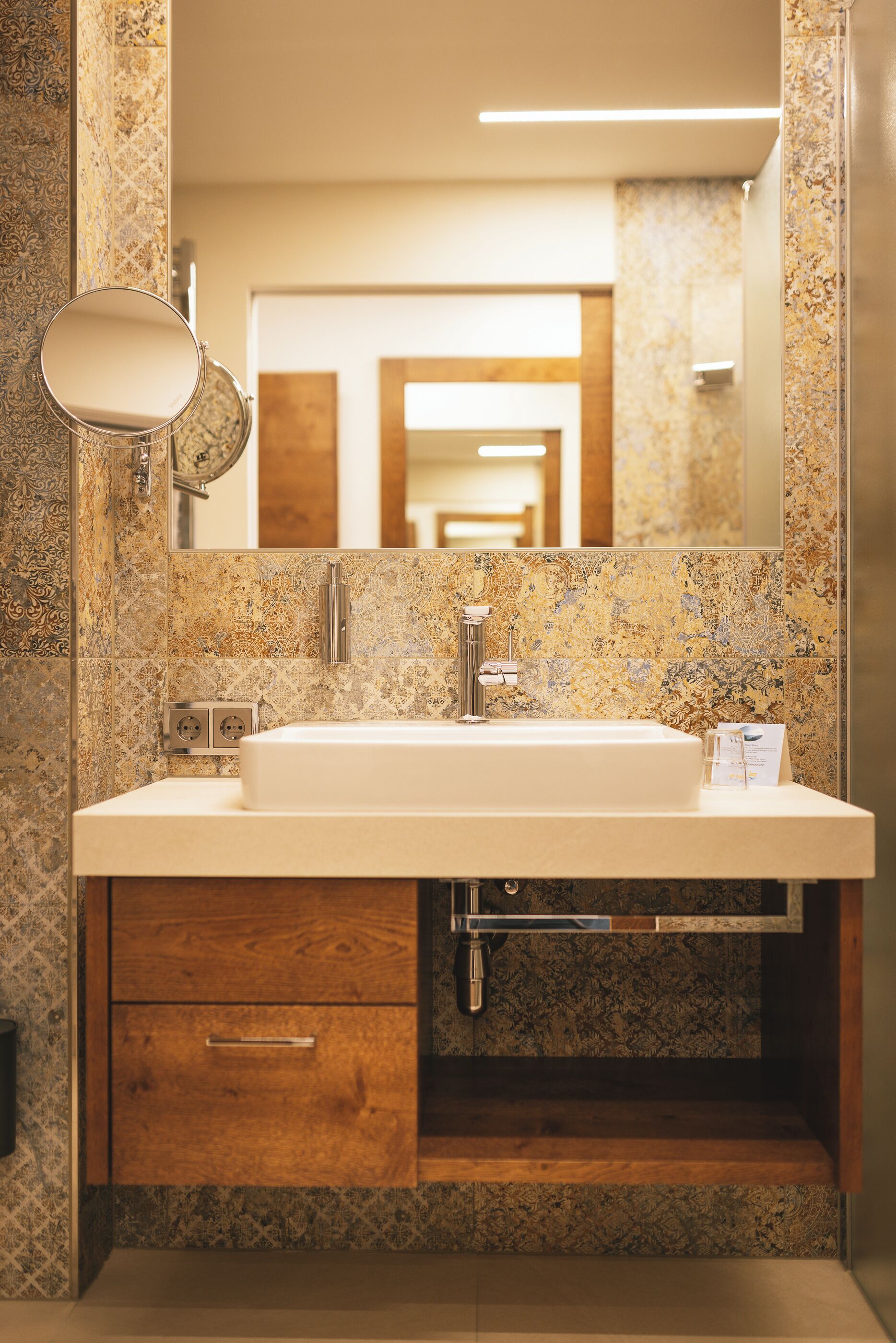 A bathroom with a marble sink, wooden cabinet, and a large mirror.