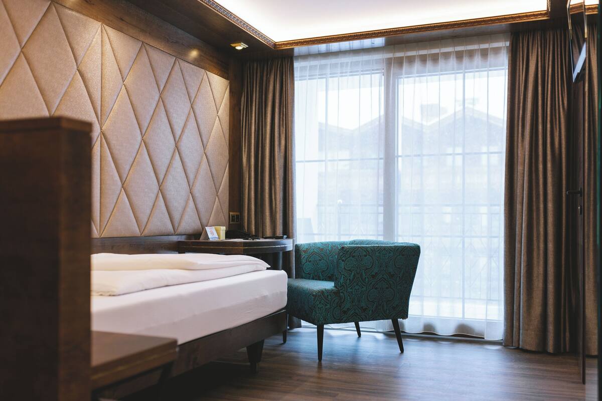 Habitación de hotel con cama, mesita de noche, silla y un amplio ventanal con cortinas.