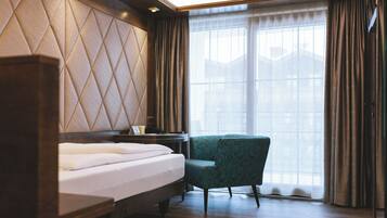 Ein Hotelzimmer mit Bett, Nachttisch, Stuhl und einem großen Fenster mit Vorhängen.
