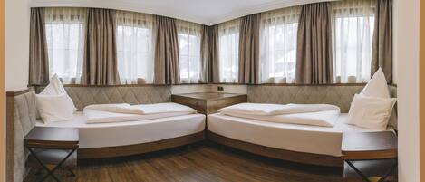 A corner room with two beds, a small table, and a window with curtains.