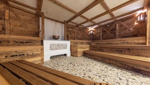 Eine Holzsauna mit Bänken, einem weißen Kamin und einem Mosaikboden.