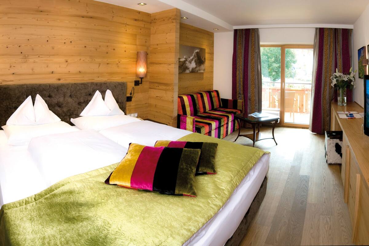 Habitación de hotel con una cama grande, televisión, paredes de madera y vistas al exterior.