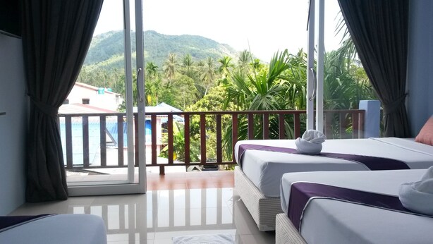 Habitación de hotel con dos camas, un balcón con vista a zonas verdes y montañas, y una puerta corredera de cristal.