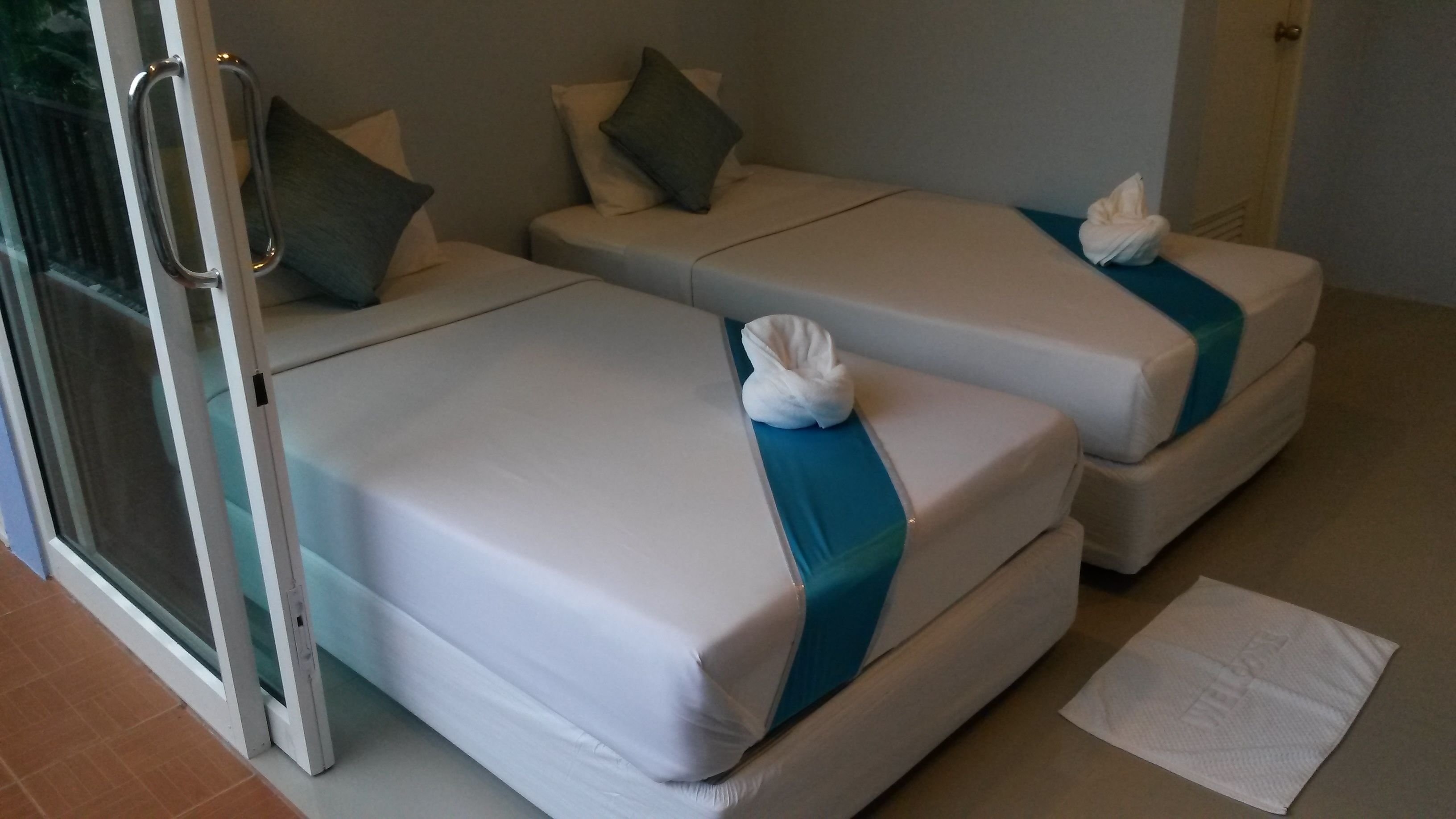 Deux lits simples avec du linge de lit blanc et bleu, une serviette sur chaque lit, et une porte vitrée donnant sur l’extérieur.