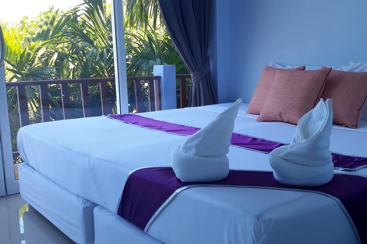 A hotel room with a bed, pillows, and a balcony with plants.