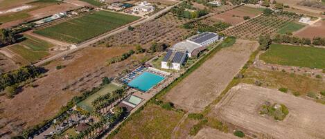 An aerial view of a resort with a swimming pool, solar panels, and various buildings.