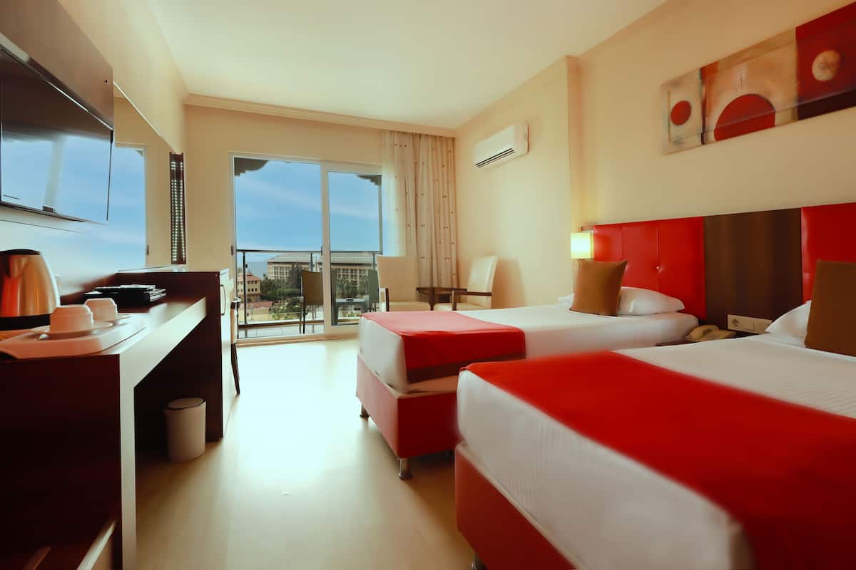 A hotel room with two beds, a desk, a chair, and a large window with a view.