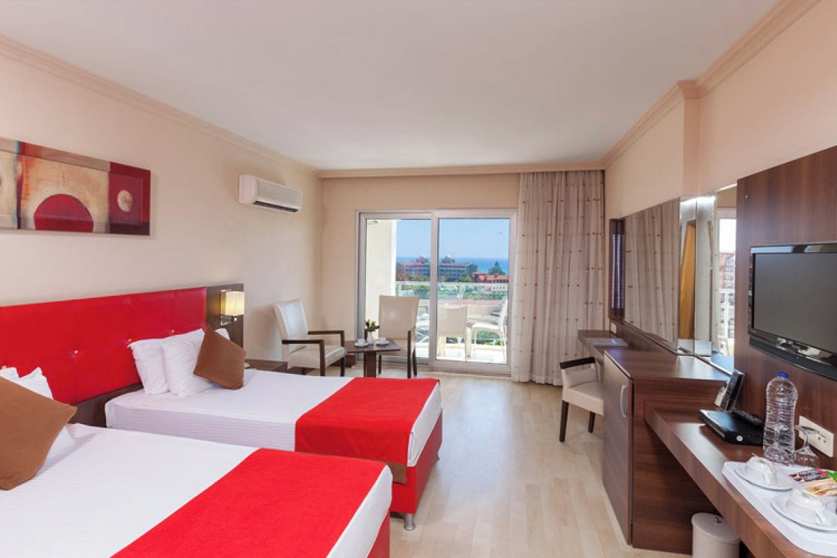A hotel room with two beds, a desk with a TV, a chair, and a view of the city.
