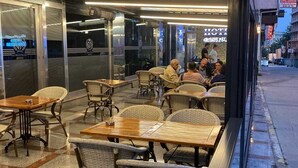 An outdoor seating area with wicker chairs and wooden tables, overlooking a street with shops and a hotel sign. - Gumus Palace Hotel (Istanbul)