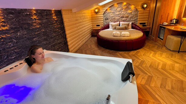 A modern spa room with a large bathtub, a stone wall, wooden paneling, and a cozy seating area with a stone fireplace. - Gumus Palace Hotel (Istanbul)