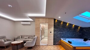 A modern spa room with a wooden floor, a sofa, a coffee table, a hot tub, and a stone wall. - Gumus Palace Hotel (Istanbul)