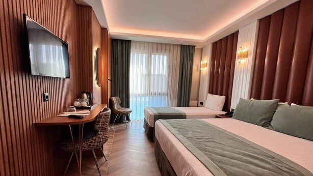 Une chambre d’hôtel avec un mur lambrissé en bois, un téléviseur à écran plat, un bureau avec une chaise, deux lits et une grande fenêtre avec des rideaux.
