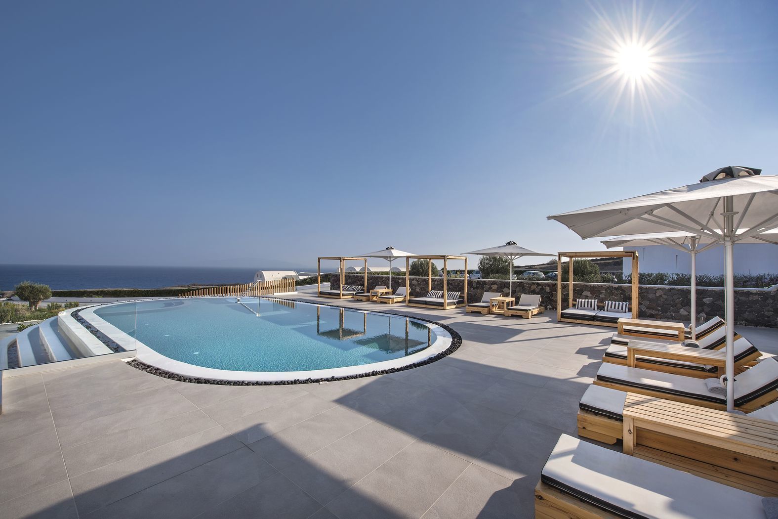 Zona de piscina con sillones de descanso y sombrillas, con vista a una masa de agua.