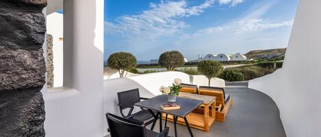 A modern outdoor seating area with a table and chairs, a stone wall, and a view of white buildings and trees under a clear sky.