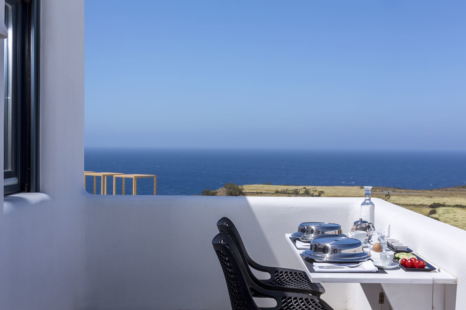 A dining table with plates, cups, and a bottle, set against a view of the ocean.