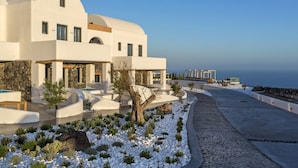 Un moderno edificio blanco con piscina, rodeado de guijarros blancos y vegetación, con vista al mar.
