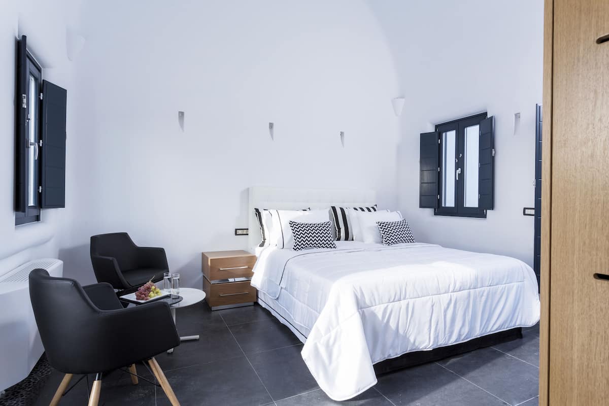 A modern bedroom with a large bed, a desk with a chair, and a small table with a fruit plate.