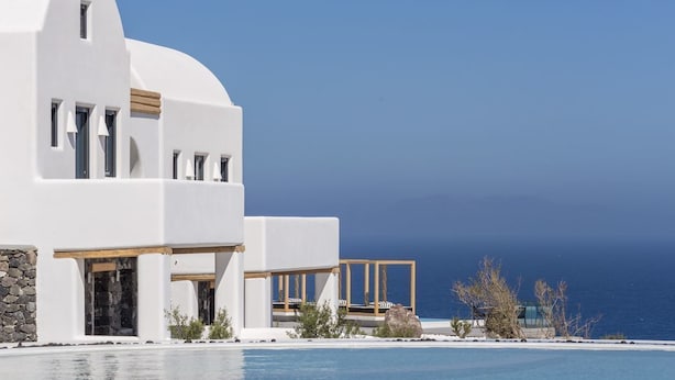 Un edificio blanco con piscina, terraza de madera y vista al océano.