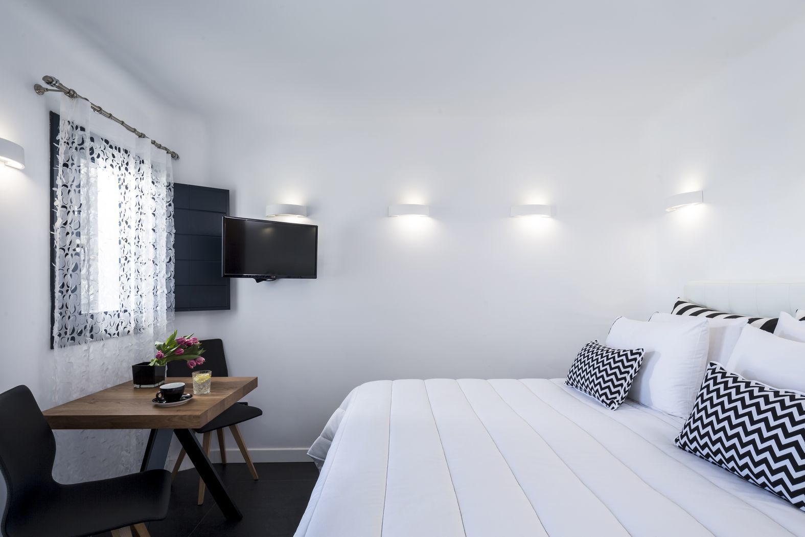 Habitación de hotel con cama, televisor montado en la pared, escritorio con silla y ventana con cortinas estampadas.