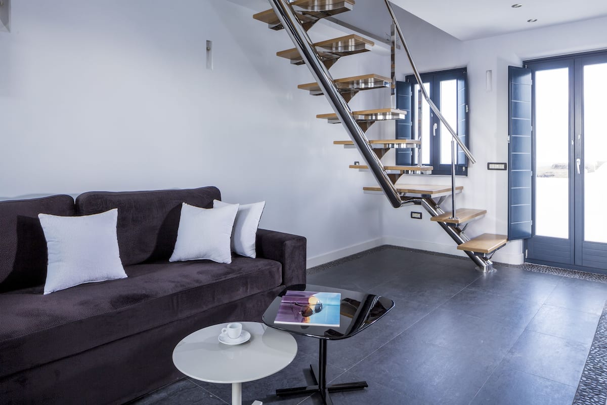 A modern living room with a dark-colored sofa, a small round table with a cup, and a unique spiral staircase.