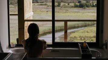 Een badkamer met een groot raam en uitzicht op het omliggende platteland.