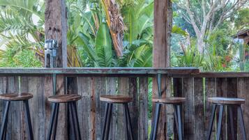 Un bar de madera rústica con cuatro taburetes, rodeado de exuberante vegetación tropical.