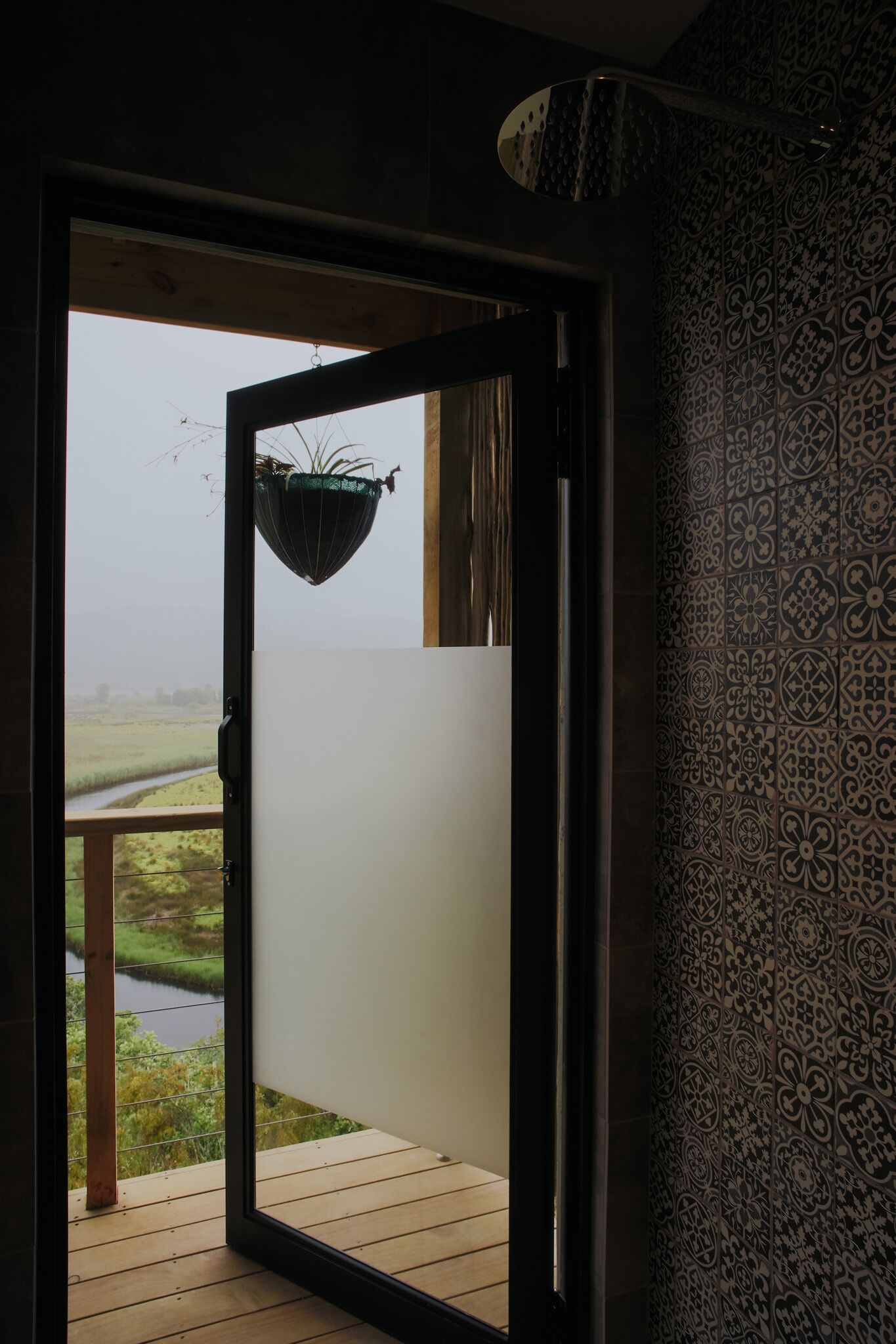 Puerta abierta que da a un balcón con vistas a un río y campos.