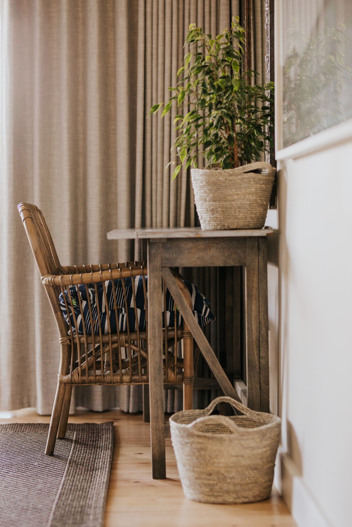 A corner of a room with a wicker chair, a woven basket, and a potted plant on a wooden table.
