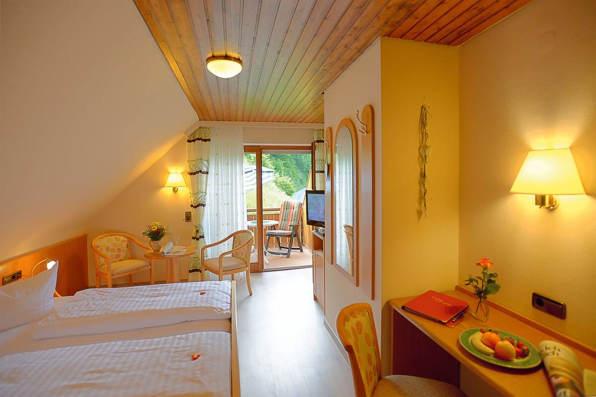 A hotel room with two beds, a desk with a laptop, a chair, a TV, and a window with curtains.