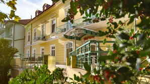 Un hotel de varios pisos con balcones, una entrada cubierta y follaje en primer plano.
