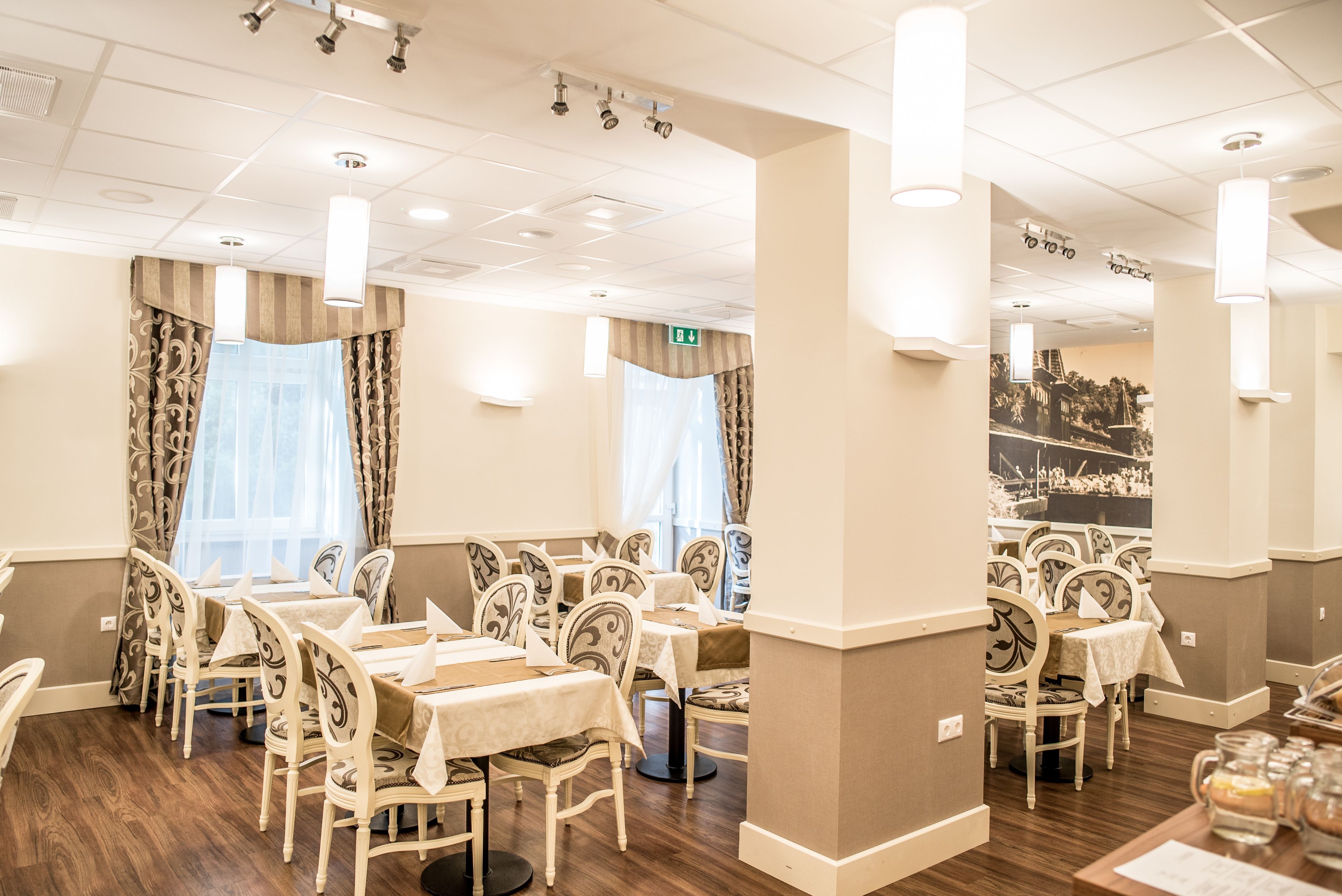 A dining area with tables and chairs, a wooden floor, and a ceiling with recessed lighting.
