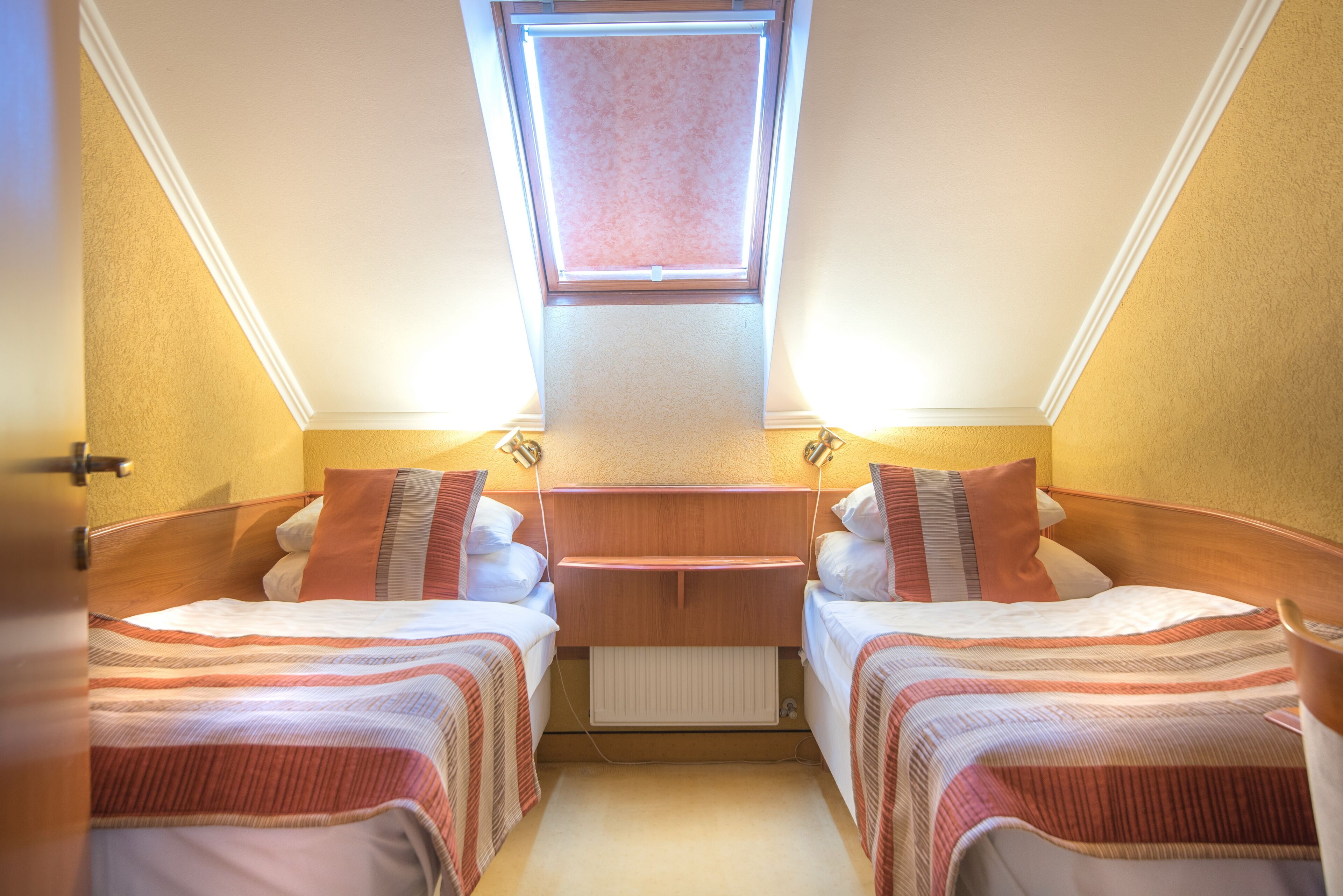 A compact room with two beds, a skylight, and a small table.