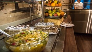 Zona de bufé con diversas opciones de comida, entre ellas frutas, postres y una ensalada de frutas.