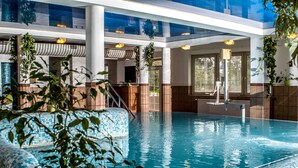 An indoor swimming pool with clear blue water, surrounded by tiled walls and large windows. - Hotel Spa Hévíz (Hévíz)
