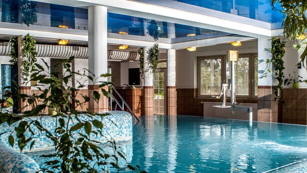 Una piscina interior con agua azul cristalina, rodeada de paredes de azulejos y grandes ventanales.