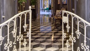 Un vaste hall d’entrée avec un sol à carreaux, des rampes blanches richement décorées et un lustre central.