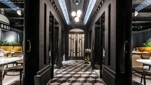 Un couloir doté d’un sol à carreaux noirs et blancs, de murs sombres et d’un plafond percé de lucarnes.