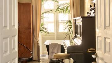 Una habitación con un piano, una silla, una planta en maceta y una ventana con cortinas.