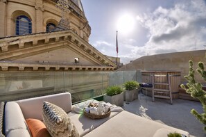 A rooftop terrace with a cushioned seating area, a wooden deck, and a view of a historic building. - Casa Ellul - Small Luxury Hotels of the World (Valletta)