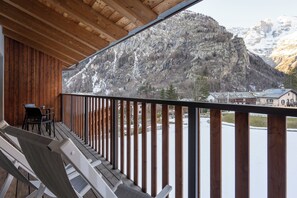 A wooden balcony with white lounge chairs and a table, overlooking a mountainous landscape with snow-covered peaks and a small building in the background. - Grand Hotel Courmayeur Montblanc by R Collection Hotels (Courmayeur)
